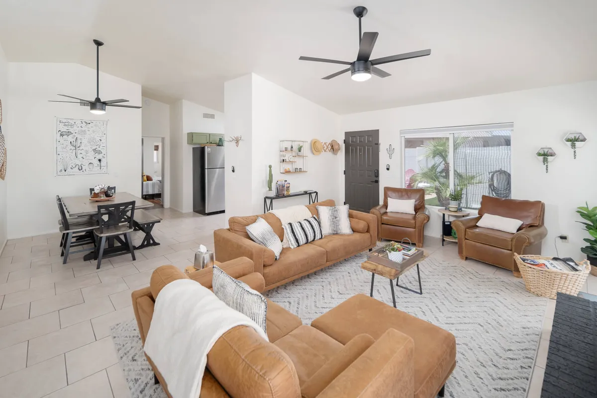 This image features a welcoming living room highlighted by comfortable brown sofas, a stylish coffee table, modern ceiling fans, and decorative wall art. The space exudes warmth, with earthy tones and plush seating inviting guests to relax or gather for conversation and entertainment.
