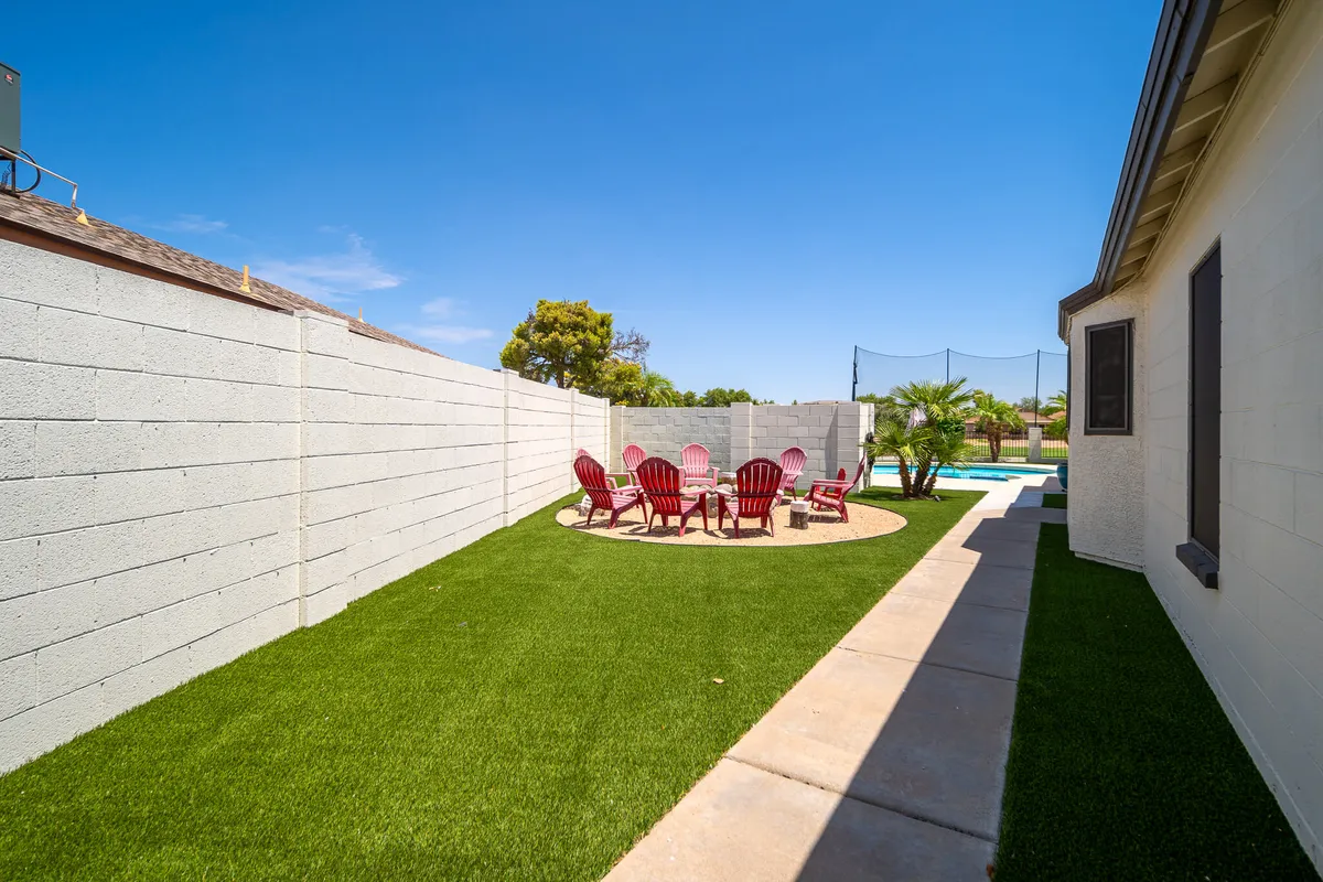 A cheerful backyard scene featuring red Adirondack chairs arranged in a circular seating area on a green lawn with a swimming pool in the background. The layout is ideal for gathering, outdoor dining, and playing yard games, offering an inviting space for families to relax together.