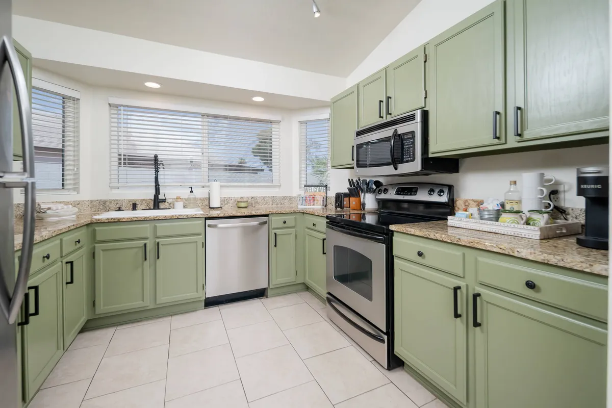 A welcoming kitchen space with sleek green cabinetry, polished granite countertops, and stainless steel appliances. The window view provides a pleasant backdrop, while the open layout promises easy flow for both cooking and social interaction.