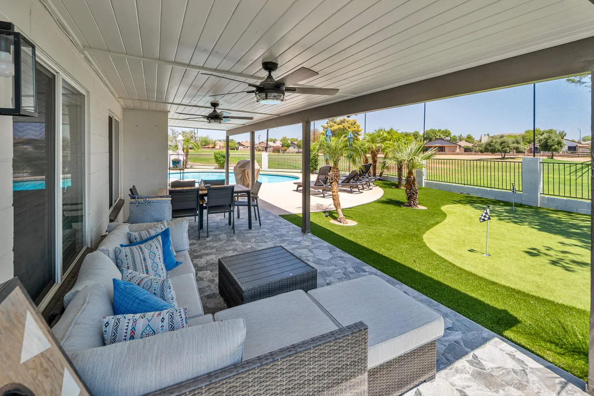 The hero image showcases a stunning backyard oasis at sunset, featuring a sparkling swimming pool surrounded by palm trees, comfortable outdoor seating for socializing, and a manicured golf putting green—all set against the serene backdrop of a golf course.
