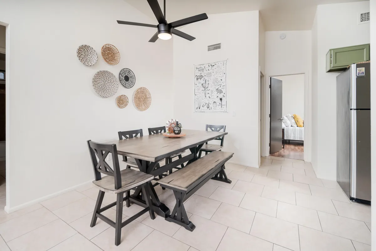 The dining area showcases a sturdy dining table with benches, decorative wall plates, a ceiling fan, and a glimpse of the refrigerator. The space balances functional comfort with inviting décor, suggesting a perfect setting for shared meals and celebrations.