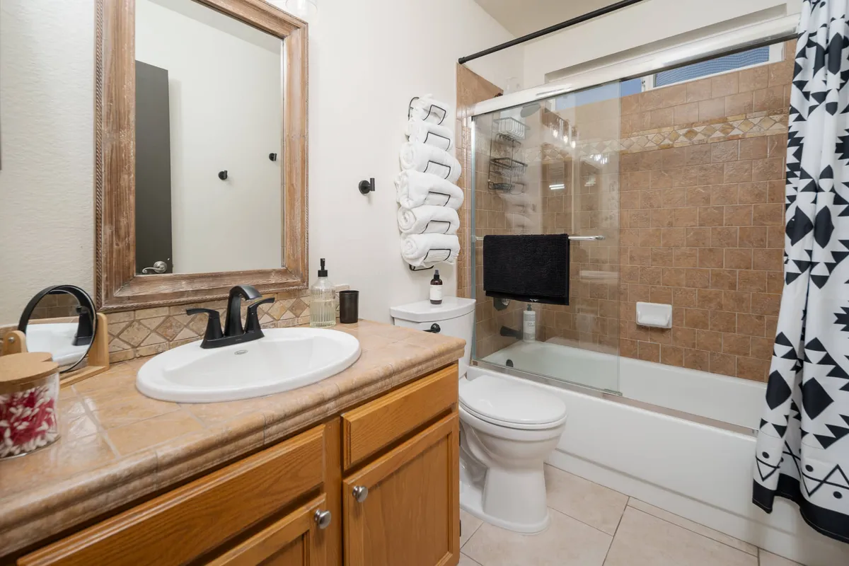 A modern bathroom featuring a vanity with a sink, a stylish framed mirror, a spacious tiled shower area, and plush towels. The space is organized and bathed in gentle light, suggesting both function and relaxation.