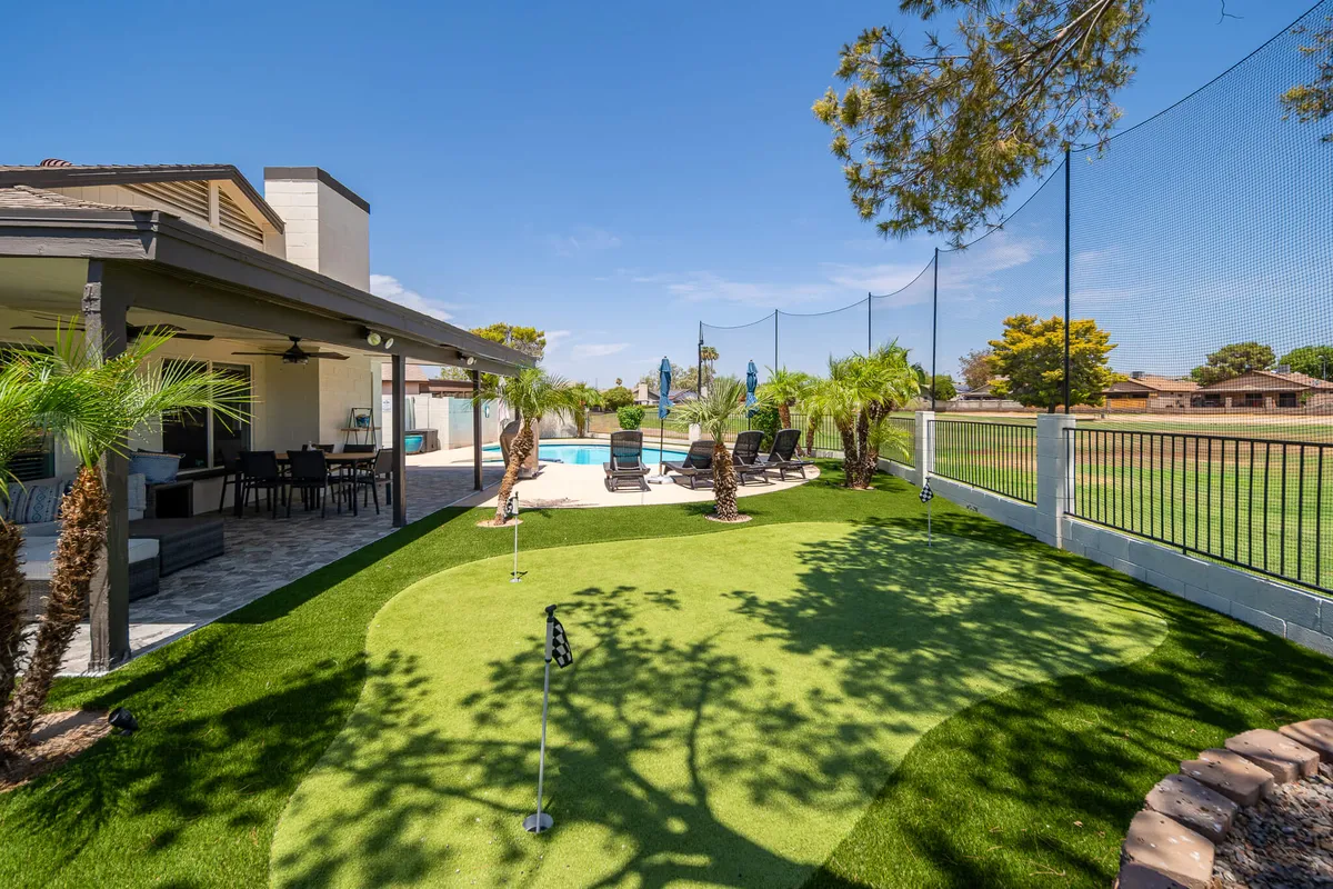 This exterior shot captures the home's putting green set beside a sparkling swimming pool, framed by palm trees and a spacious patio area. Sun loungers and open sky suggest both recreation and relaxation, blending golf practice with the pleasures of outdoor living.